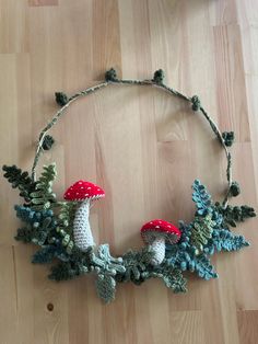 a crocheted necklace with two mushrooms and pine cones on it sitting on a wood floor