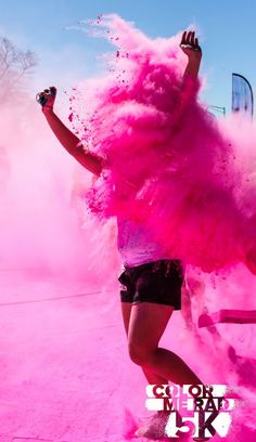 a woman with pink powder on her face and arms, running through the air in front of a bus