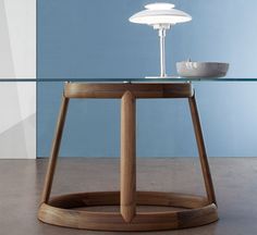 a glass table with a wooden base and light fixture on the top, in front of a blue wall