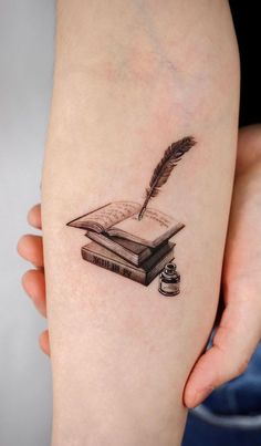 a person with a tattoo on their arm holding a book and a feather quill