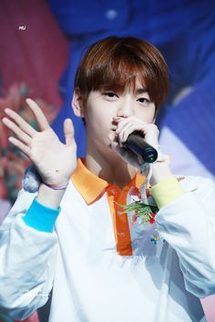 a young man holding a microphone up to his mouth while wearing an orange and white shirt