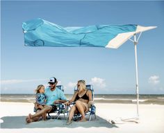 a man and two women sitting under an umbrella on the beach