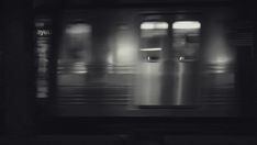 a black and white photo of a train passing by at night with the door open