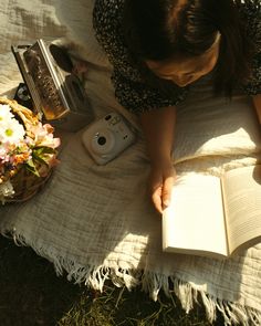 a woman reading a book while laying on the grass with her camera next to it