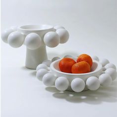 a white bowl filled with oranges on top of a table next to a vase