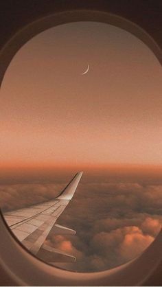 an airplane window looking out at the sky and clouds with a half moon in the distance