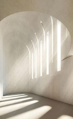 the sun shines through an arch in a white room with concrete walls and flooring