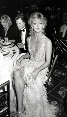 black and white photograph of woman in feather dress sitting at table with man looking on