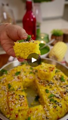 someone holding up a piece of cake in front of a pan with other food on it