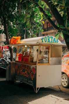 a food cart parked on the side of the road next to a tree and cars