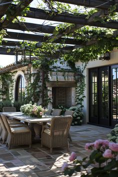 an outdoor dining table and chairs under a pergolated roof with flowers in the foreground