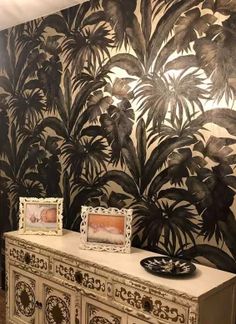 a white dresser sitting in front of a wall covered in black and white palm leaves