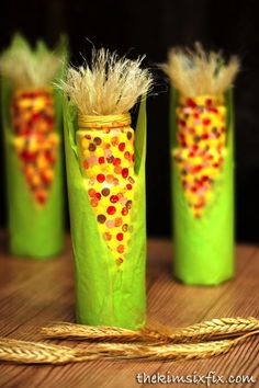 three green vases decorated with corn on the cob and some grass in them