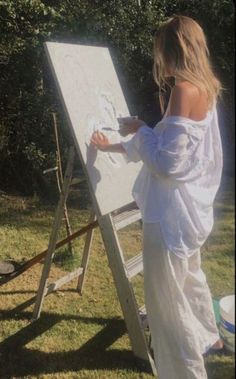 a woman standing in front of a white easel drawing on the grass with her hands