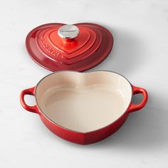 a red pot with a heart shaped lid next to a white pan filled with liquid