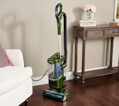 a green vacuum is on the floor in front of a white chair and end table