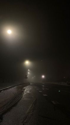 the street is covered in snow and fog at night with three lights shining on it