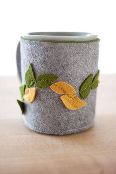 a felt mug with leaves on it sitting on a table next to a cup holder