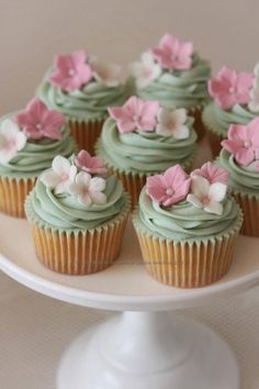 cupcakes with green frosting and pink flowers on top sitting on a cake plate