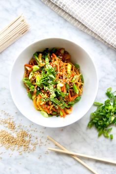 a white bowl filled with vegetables on top of a table next to chopsticks