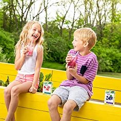 two young children sitting on a yellow bench eating ice cream and drinking milk from cups