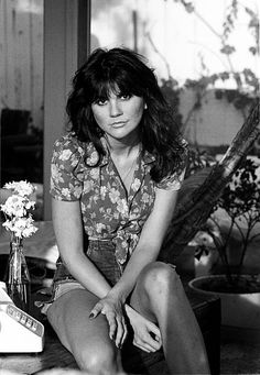 a black and white photo of a woman sitting on a table with flowers in a vase