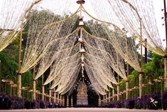 an outdoor ceremony with white draping and purple flowers on the ground, surrounded by tall trees