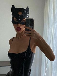 a woman taking a selfie in a cat mask and latex outfit with her cell phone