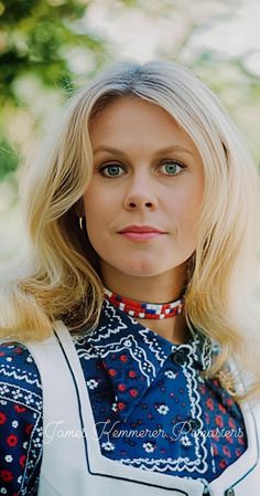 a woman with blonde hair wearing a blue and white dress standing in front of trees