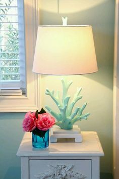 a table with a lamp and some flowers on it in front of a white dresser