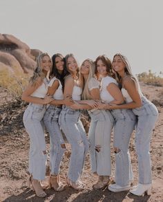 four women in white tops and jeans are posing for a photo with their arms around each other