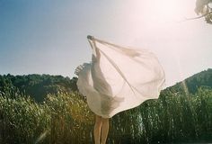 a woman is walking in the grass with a white cloth over her head and body