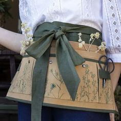 a woman is wearing an apron with flowers on it and scissors in the back pocket