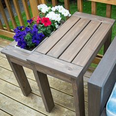 a wooden table sitting on top of a wooden deck next to a planter filled with flowers