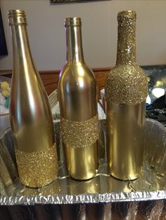 three champagne bottles sitting on top of a metal tray covered in gold flecks