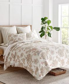 a bed with a white comforter and pillows on top of it next to a potted plant