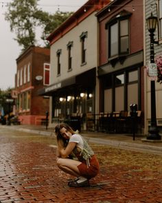 a woman kneeling down on the ground in front of a building holding her face to her chest