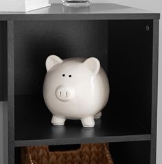 a white piggy bank sitting on top of a book shelf next to a basket