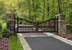 a gated driveway with flowers and trees in the background, surrounded by stone pillars