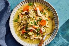 a bowl filled with chicken noodle soup on top of a blue cloth next to a wooden spoon