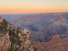 the sun is setting at the edge of the grand canyon, with cliffs in the foreground