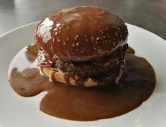 a hamburger covered in chocolate sauce on top of a white plate