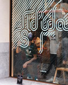 a man sitting on a bench in front of a store window with the words adidas printed on it