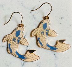 two fish shaped earrings sitting on top of a marble countertop next to each other