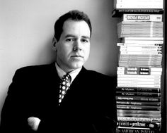 a man in a suit and tie leaning against a wall with books stacked on it