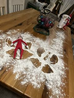 a wooden table topped with lots of snow covered ground next to an elf figurine