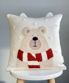 a white pillow with a bear on it sitting on a wooden stool in front of a gray wall