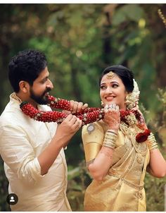 a man and woman standing next to each other in front of some trees holding beads