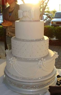 a white wedding cake sitting on top of a table next to a woman in front of a window