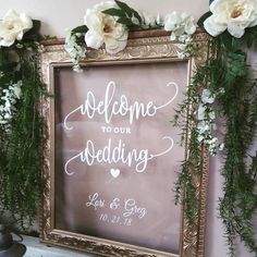 a sign that says welcome to our wedding with flowers and greenery on the wall